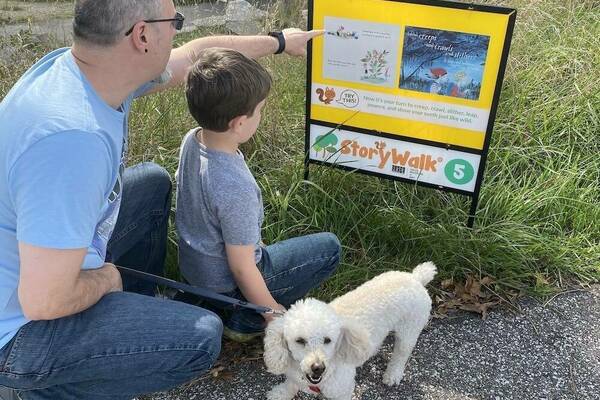 Image of adult and child with their dog looking at a sign about StoryWalk.
